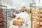 Bearded baker smiles holding a basket of bread at the bakehouse