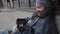 Bearded begging man sitting in street with smartphone.