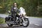 Bearded biker in black leather jacket on modern motorcycle on country roadside.