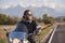 Bearded biker in black leather jacket on modern motorcycle on country roadside.