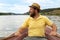 A bearded boatman in a hat looks at the shore while sitting in a boat and holding the oars in his hands