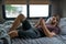 A bearded brown haired hypster man wearing a red t-shirt lays down laughing relaxing on his bed in his camper talking to someone