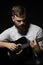 Bearded brutal guitarist plays an acoustic guitar in a black room.