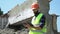 Bearded builder in a helmet and reflective vest uses a tablet on the background of a destroyed building, preparing for