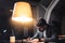 Bearded businessman sits by the wooden table with lamp and working on new startup project in loft ofiice at night