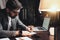 Bearded businessman sitting in night loft office and working with documents and contemporary laptop. Stylish man with glasses sits