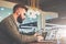 Bearded businessman sitting at table in cafe,holding smartphone and using laptop with charts,graphs on screen.