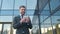 A bearded businessman stands on the background of a business center and counts a pile of money