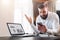 Bearded businessman in white shirt is sitting at table in front of laptop with graphs, charts, diagrams on screen