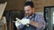 Bearded carpenter works with wooden bar in workshop.