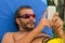 Bearded Caucasian man with sunglasses using smartphone on a sunbed in a resort