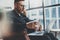 Bearded coworker working at the modern workplace.Man sitting in vintage chair,holding in hands glass of water,using