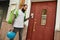 Bearded delivery man with thermo backpack using smartphone, standing by the door, while completing the order. Courier