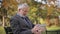 Bearded elderly man in glasses reading newspaper in the autumn park. Handsome gray-haired man sitting on the bench early