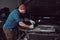 A bearded expert mechanic dressed in a uniform, standing with crossed arms against a car in the garage.