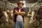 Bearded farmer with hat and gloves posing with crossed arms on a cattle farm