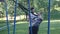 Bearded fitness trainer controls young man intense doing pull-ups on fitness loops in summer park. 4K slow mo footage