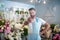 Bearded florist in apron spraying water at camera inside flower shop