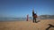 Bearded guitarist in black plays on beach by girl in red