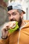 Bearded guy eats fast food. Burger is not helpful food. Very hungry guy. Hunger Man eat Hamburger outdoor. Man eat tasty