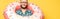 Bearded guy in glasses with donut swim ring isolated on yellow, panoramic orientation