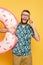 Bearded guy in glasses with donut swim ring talking on smartphone on yellow