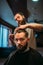Bearded hairdresser making male hipster hairstyle