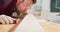 A bearded handyman is sanding wood for furniture in a carpentry workshop The carpenter blows off the chips after sanding