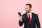 Bearded happy male in suit and red tie looks at smartphone on pink background. Businessman makes video chat with clients