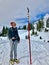 Bearded hiker man looking at Grey Jay perched on pole mark in winter mountains.