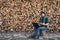 Bearded hipster freelancer in headphones working on laptop and uses phone against background of firewood wall