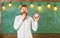 Bearded hipster holds clock, chalkboard on background, copy space. Forgot about time concept. Teacher in eyeglasses