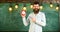 Bearded hipster holds clock, chalkboard on background, copy space. Man with beard and mustache on smiling face stands in