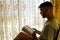 Bearded hispanic man reading a book close to the window