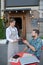 Bearded male paying bill with smartphone in open air cafe, waitress holding payment terminal