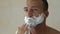 Bearded man applying shaving cream in front of mirror in bathroom, new style