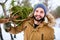 Bearded man carrying freshly cut down christmas tree in forest. Young lumberjack bears fir tree on his shoulder in the