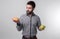 Bearded man in checkered shirt on a light background holding a hamburger and an apple. Guy makes the choice between fast