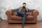 Bearded man with confident face sit leather couch. Loft interior apartment. Businessman realtor work. Furniture shop