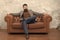 Bearded man with confident face sit leather couch. Loft interior apartment. Businessman realtor work. Furniture shop