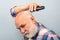 Bearded man cutting his own hair with a clipper. Man hair treatment. Gray man hair clippings. Bald man hairclipper