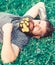 Bearded man with dandelion flowers lay on meadow, grass background. Hipster with bouquet of dandelions in beard relaxing