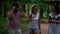 A bearded man with dark glasses and two different dark-haired girls are walking through the forest and talking, laughing