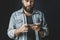 Bearded man in denim shirt holding smartphone in hands and texting. Young hipster using mobile phone for online communication