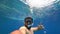 Bearded man engaged in scuba diving floats to the surface of the sea and shows a victory sign