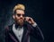 A bearded man with expressive style dressed in a violet elegant suit standing against a dark textured wall