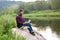 Bearded man, freelancer sitting with a laptop by the river, remote work concept