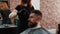 Bearded man getting haircut in chair in barbershop. Woman cutting hair with scissors of hipster man in barber salon