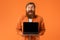 Bearded Man Holding Laptop Computer With Empty Screen, Orange Background