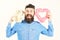 Bearded man holds symbols of love. Hipster with heart, teddy bear and happy joyful face. Macho with beard smiles